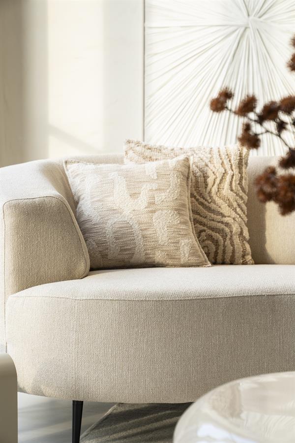 By Boo Sebra zand met streepdessin naast een licht grafisch kussen op een beige fauteuil